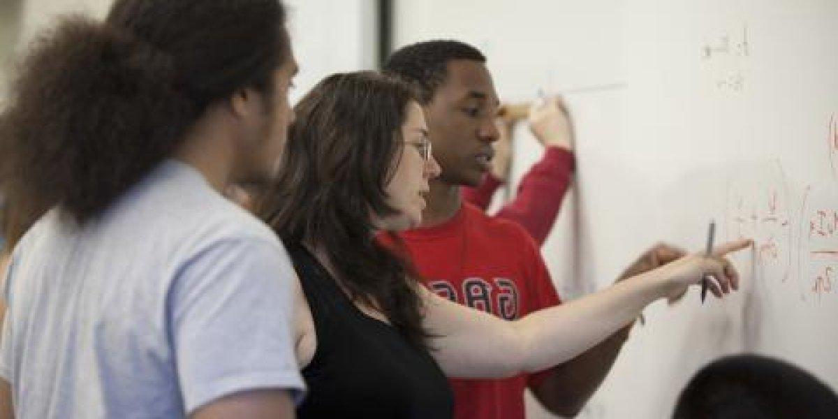 Students standing at whiteboard working on an equation