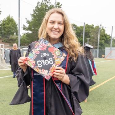 A graduate holding a cap that says Miss Berg