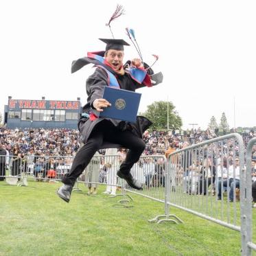 Graduating student jumping holding a diploma