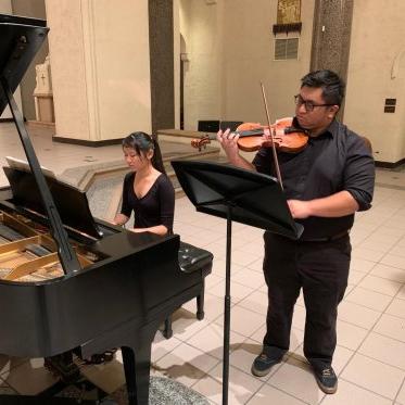 A shot of two chamber musicians, 一个拉小提琴，另一个弹钢琴, performing at the Chapel