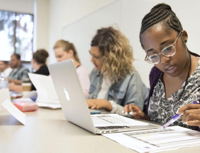 Professional MBA students sitting at a row of desks doing work on laptops and paper