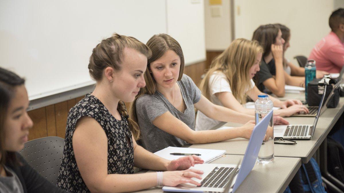 2 students in class looking at one laptop screen