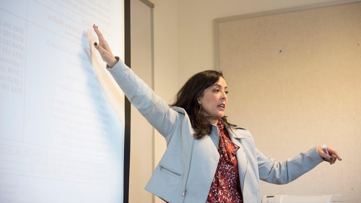 A professor gesturing to a projection while teaching